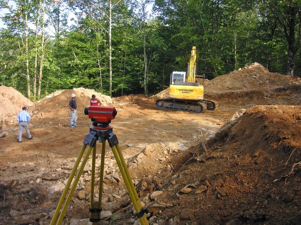 Survey equipment and excavator at a construction site with workers in a forested area